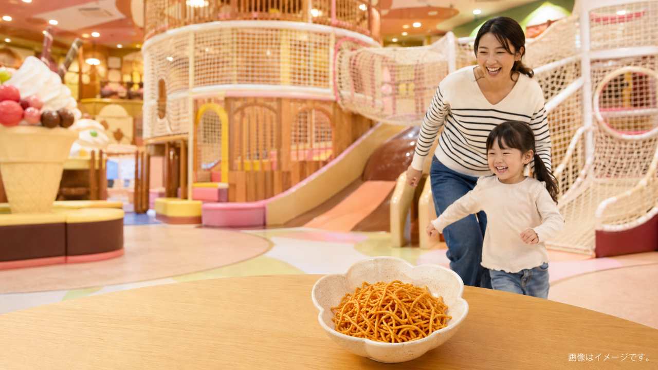 三重県の屋内型お菓子テーマパークをイメージした明るくカラフルな空間、巨大なネット遊具やスライダーを背景に楽しそうに遊ぶ日本人の親子